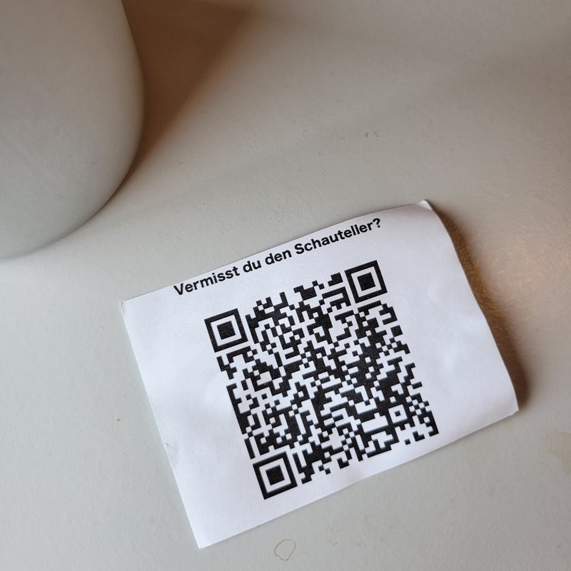 Kleiner Papierzettel mit einem QR-Code, der auf einem Tisch liegt. 